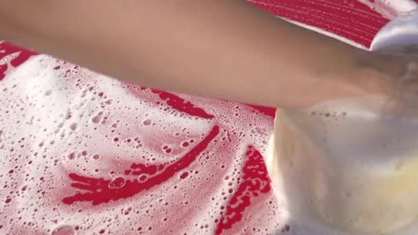 Nainen pesee punaista autoa sienellä
 - Materiaali, video