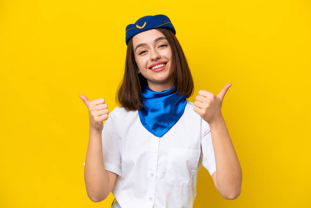 Vliegtuig stewardess Oekraïense vrouw geïsoleerd op gele achtergrond met duimen omhoog gebaar en glimlach - Foto, afbeelding
