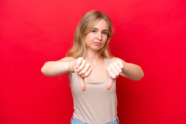 Young English woman isolated on red background showing thumb down with two hands - Фото, зображення