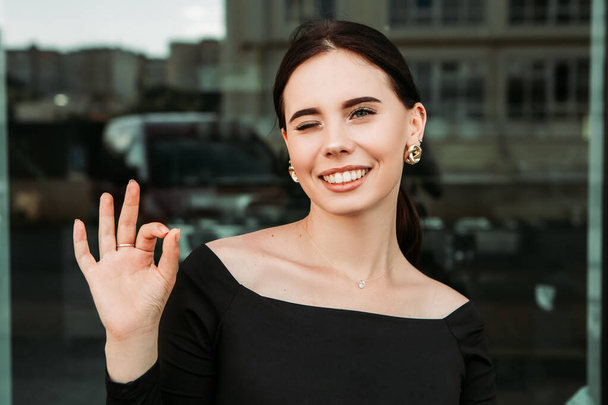 Pretty brunette caucasian woman standing outside street with white teeth beaming healthy smiling lady. Happy millennial girl model showing OK approve sign gesturing making faces - Φωτογραφία, εικόνα