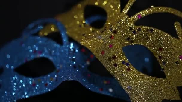 Two luxury traditional venetian masks on dark background illuminated and sparkles from the darkness. Blue and gold shiny carnival masquerade fantasy mask with small colorful stars under light in dark - Felvétel, videó