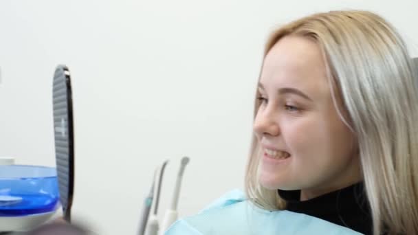 Tyytyväinen potilas katsoo parantuneita hampaita hammaspeilistä. Hammashoidon tulos. Terve suuontelo - Materiaali, video