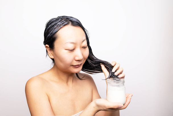 Посмішка молода азіатка, що використовує маску для волосся у ванній кімнаті; ідея догляду за волоссям. - Фото, зображення