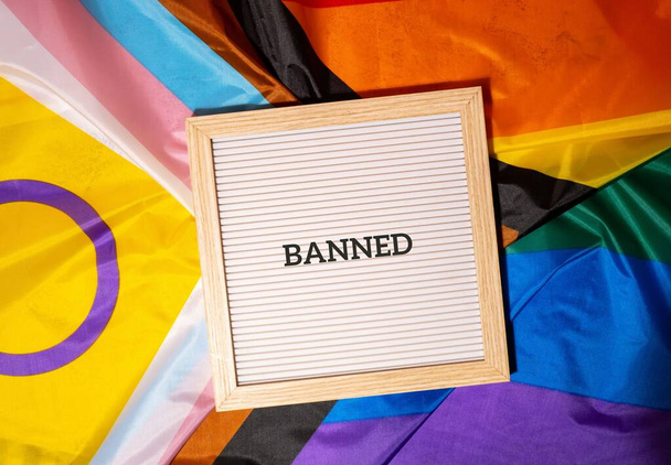 BANNED text frame on Rainbow LGBTQIA flag made from silk material. Символ месяца гордости ЛГБТК. Равные права. Мир и свобода. Поддержка ЛГБТКИИ сообщества. Равенство разнообразия - Фото, изображение