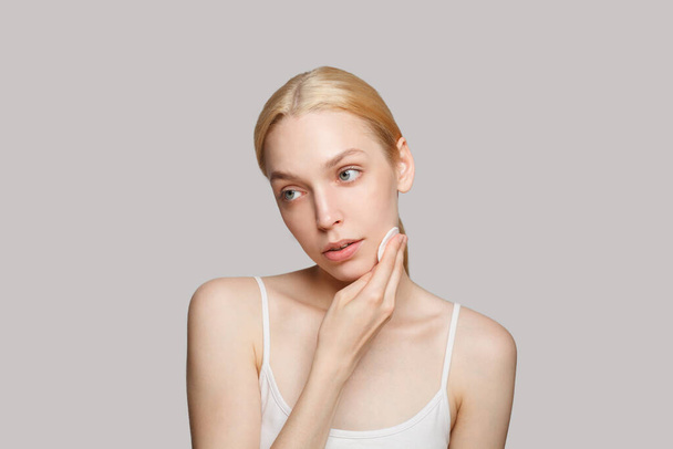 Evening routine concept. Young blonde woman is removing makeup using cotton pad - Foto, Imagen