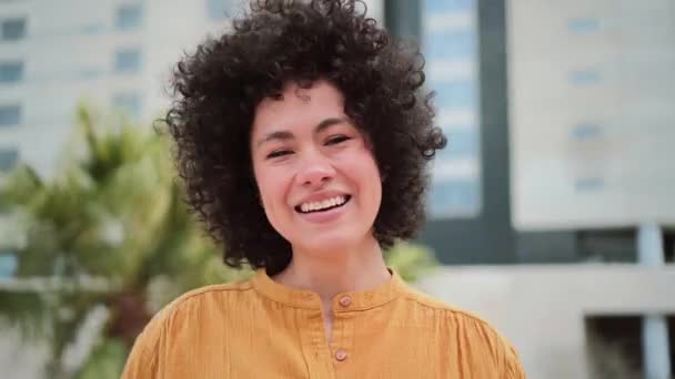 Front view of happy young hispanic woman smiling, tauching her curly hair and throwing a kiss to the camera. Close up portrait of cracy lady laughing and having fun and doing mad things. High quality - Záběry, video