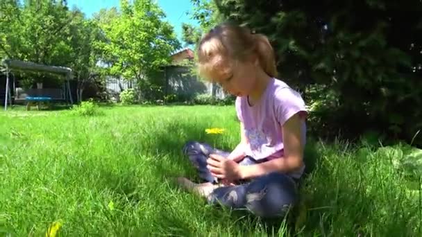 Portrait of a little sad girl sits on the lawn under the spruce. High quality 4k footage - Filmmaterial, Video