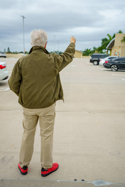 駐車場で車を探している老人は、彼の足のロックを解除ボタンを押すことで - 写真・画像