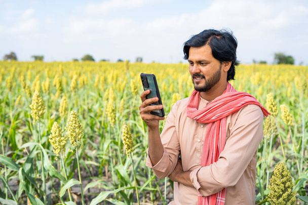 Farmer busy using mobile phone at agricultural farm land showing with copy space - concept of technology, connection and modern village farmer. - Foto, Imagem