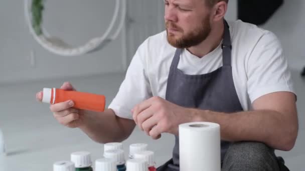 A talented confident focused artist shake and uncorks a tube of orang paint. The male artist begins the process of creating a painting.  - Materiał filmowy, wideo