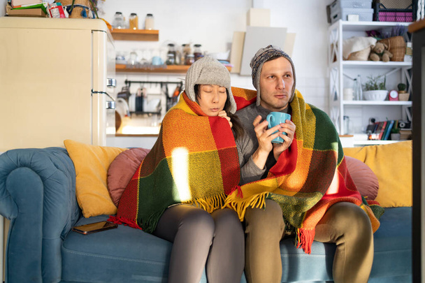 Couple cold on sofa at home with winter coat in a blanket. - Photo, Image
