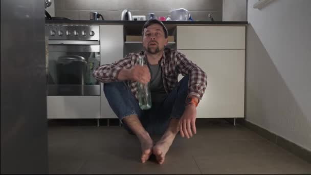 Drinking alone. Concept of male drunkenness, bad habits, addiction, depression. Drunk unhappy male drinks wine from a bottle sitting on the kitchen floor at home in the evening. Alcohol dependence.  - Záběry, video