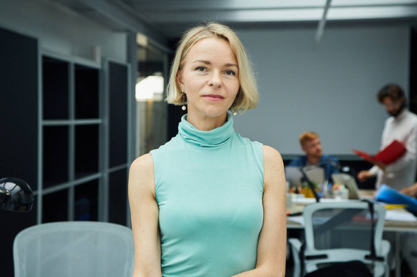 Serious confident blonde Caucasian business woman looking at camera standing in office. Executive CEO professional middle aged female manager posing for business portrait. Senior people at work place - Fotoğraf, Görsel