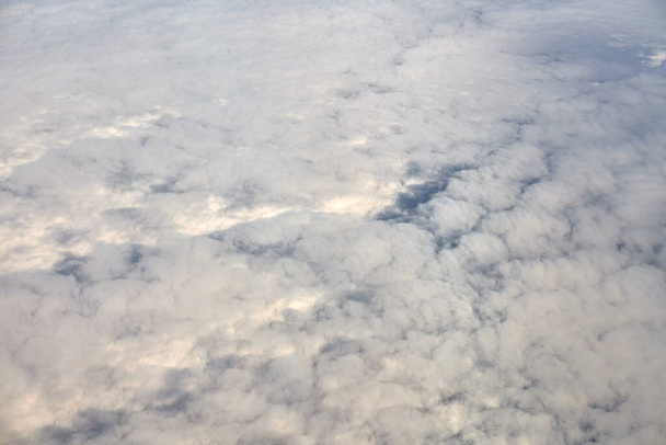 Over clouds aerial top view from aircraft window, thick white blue clouds looks like soft foam, overcast with fresh frosty air. Beautiful cloudy sky view to troposphere, heavy cloudiness - Foto, Bild