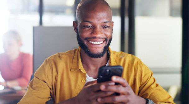 Black man, phone and office chat while online for communication, social media or reading email, news or content creator post. Smile on face of employee at desk for project research on website. - Foto, afbeelding