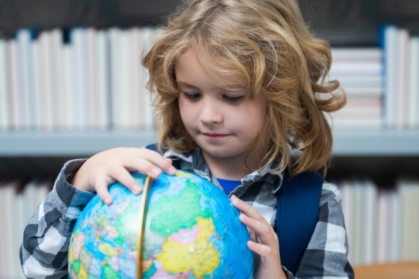 Alumno mirando el globo en la biblioteca de la escuela primaria. Niño nerd de la escuela. Un niño inteligente de la escuela primaria con libro. Un genio inteligente listo para aprender. Mundo globo - Foto, imagen