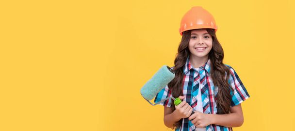 happy child with curly hair in construction helmet hold paint roller, painting. Child builder in helmet horizontal poster design. Banner header, copy space - Fotografie, Obrázek