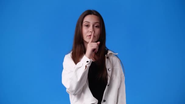 4k slow motion video of one girl showing silence sign over blue background. Concept of emotions. - Imágenes, Vídeo