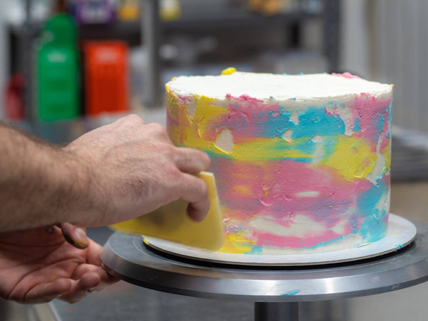 шеф дизайнер кондитерських виробів, що конфігурує матовий 3 поверх шаруватий торт, прикрашений пастельними кремовими кольорами фото
. - Фото, зображення