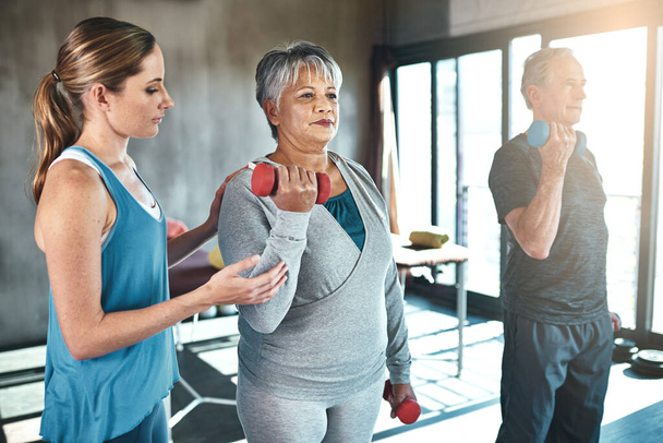 Hora de levantarse y ponerse en marcha. un hombre y una mujer mayores que usan pesas con la ayuda de un fisioterapeuta - Foto, imagen