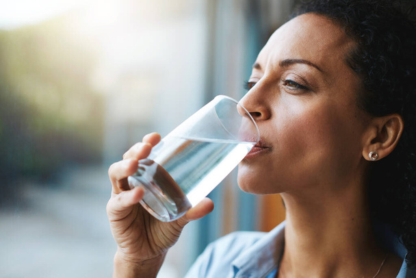 Blijf kalm en hydrateer. een vrouw die thuis een glas water drinkt - Foto, afbeelding