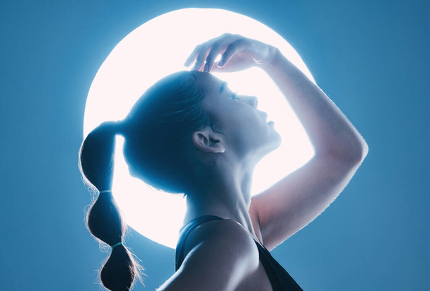 Beauty, light and profile of a model in a studio with a sensual, soft and attractive pose. Cosmetic, magical and slim woman with a mystical glow posing by a moon while isolated by a blue background - Foto, immagini