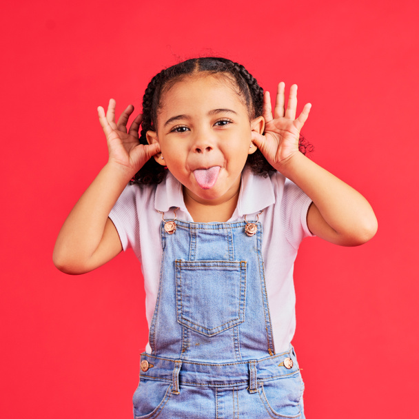 Child, portrait and tongue out on isolated red background in goofy, silly games and playful facial expression. Happy, kid and little girl with funny face in comic emoji, charades and studio activity. - Photo, image