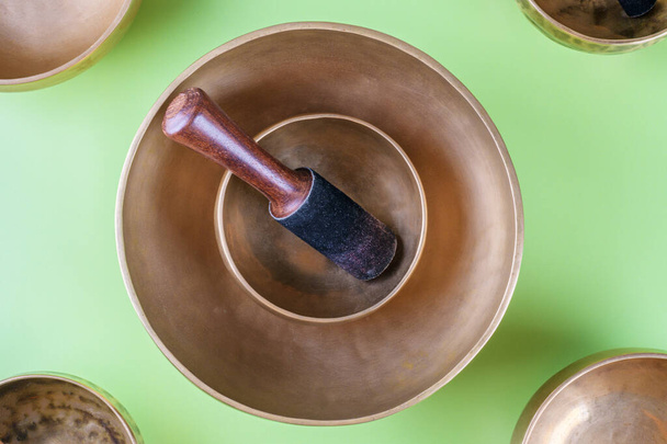 Tibetan singing bowls with stick used during mantra meditations on green background, top view, flat lay. Sound healing music instruments for meditation, relaxation, yoga, massage, mental health - Photo, image