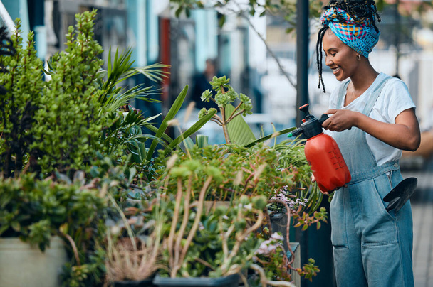 Water, flowers or black woman gardening in small business shop for healthy leaf or organic plants growth. Irrigation, store manager or girl entrepreneur watering floral agriculture with a happy smile. - Foto, imagen