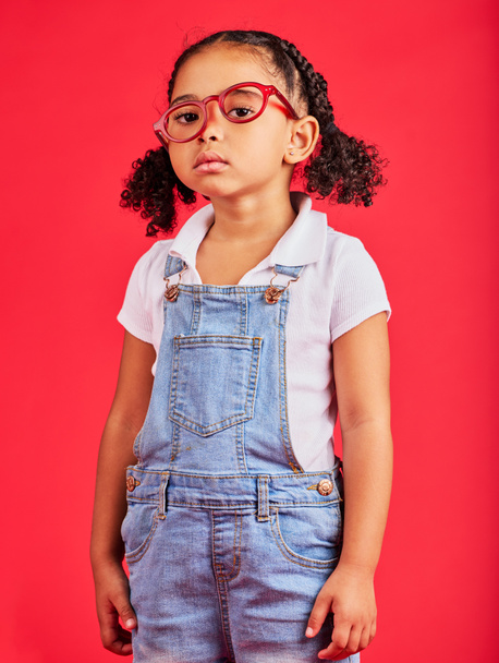 Portret, bril en ongelukkig met een zwart meisje op een rode achtergrond in de studio voor zicht of gezichtsvermogen. Kinderen, verdrietig of verveeld met een vrouwelijk kind dragen een nieuw frame recept bril voor correctie. - Foto, afbeelding