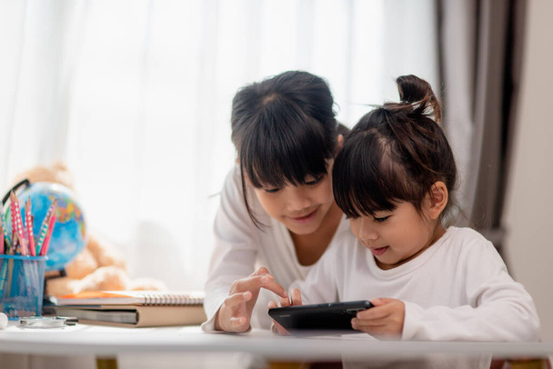 Koncepcja dzieci i gadżety. Dwie dziewczynki rodzeństwo Siostry patrzą na telefon i uśmiechają się. Trzymają filmy ze smartfonami, uczą się, grają w gry, mówią online. Internet dla dzieci. Kontrola rodzicielska - Zdjęcie, obraz