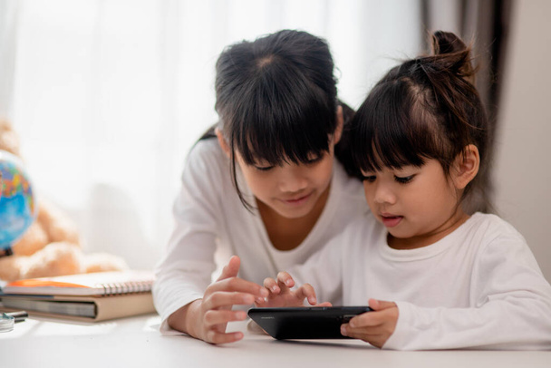 Concept enfants et gadgets. Deux petites filles sœurs sœurs regardent le téléphone et sourient. Ils tiennent un smartphone regarder des vidéos, apprendre, jouer à des jeux, parler en ligne. Internet pour les enfants. Contrôle parental - Photo, image