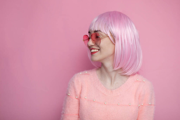 young cute girl with pink short hair looks away on a pink background and smiles - Foto, Imagen