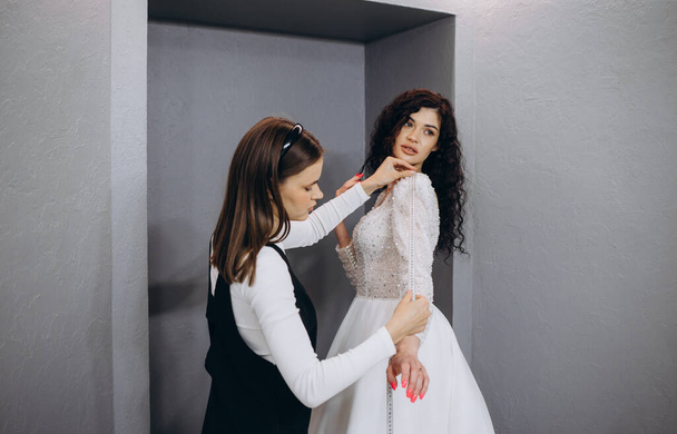 Female making adjustment to wedding gown in fashion designer studio. Bride wearing her wedding gown with female dress designer making final adjustments on dress. - Fotografie, Obrázek