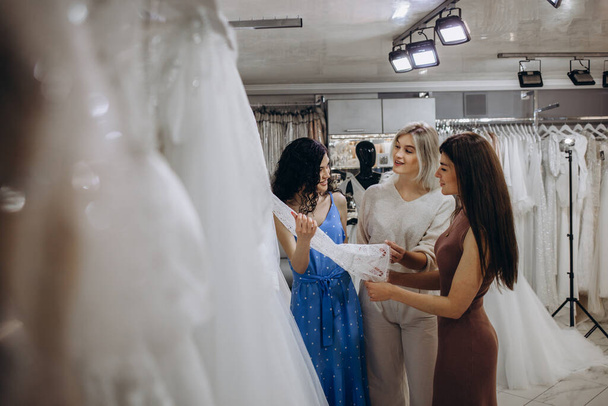 Three girlfriends - A Bride-To-Be and bridesmaid Trying On A Wedding dress - Photo, image
