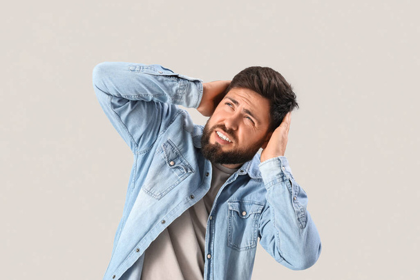 Young man suffering from loud noise on grey background - Foto, immagini