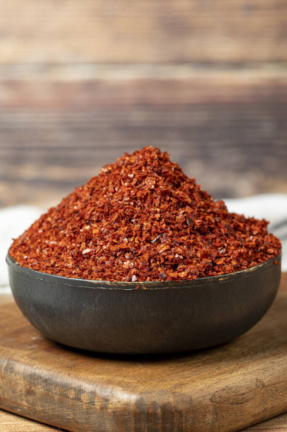 Red pepper flakes. Crushed chili pepper in bowl, dried chili flakes on wooden background. Close up - Foto, afbeelding