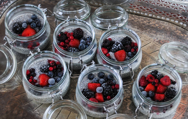Six glass bowls of chia seeds pudding with mixed fruit berries on silver tray background - 写真・画像