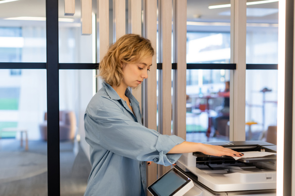 young blonde woman with wavy hair using modern printer in office  - Photo, Image