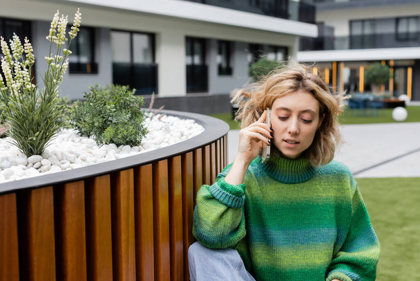 Молода блондинка в зеленому светрі розмовляє на смартфоні біля готелю в Барселоні.  - Фото, зображення