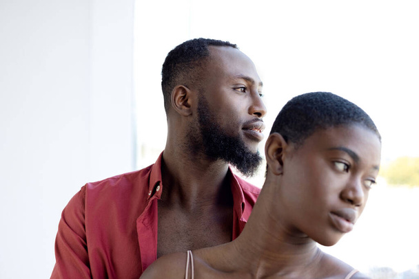 African American couple with short hair cuddling near window on sunny day. Woman and man looking away, breaking up romance affair concept. Horizontal copy space - Foto, Imagem
