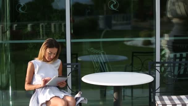 Young beautiful business woman sitting at a table with tablet in hands - Materiał filmowy, wideo