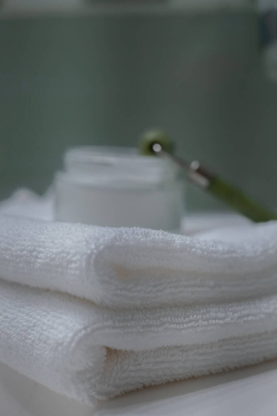 Stack of fresh towels, face roller and cream on countertop in bathroom - Foto, afbeelding