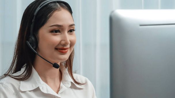 Asian customer support operator wearing headset and microphone working at her desk with laptop. Enthusiastic female employee provide customer service, supportive call center agent helping customers. - Photo, Image