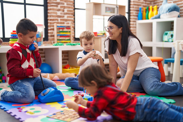 Вчителька з групою хлопчиків, які грають з іграшками, сидячи на підлозі в дитячому садку
 - Фото, зображення