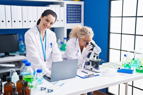 Twee vrouwelijke wetenschappers met microscoop en laptop in het laboratorium - Foto, afbeelding