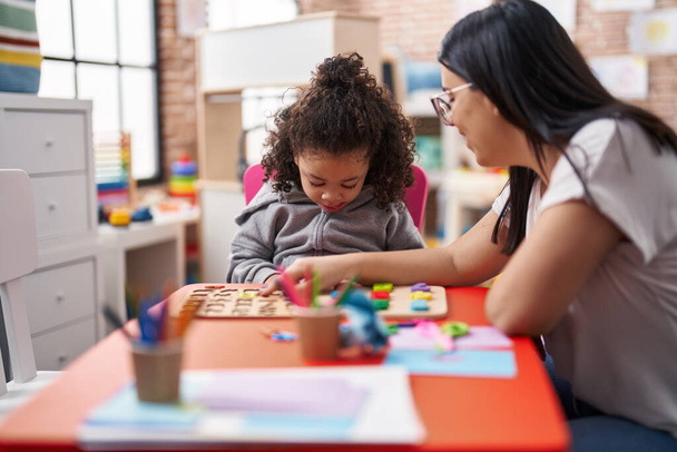 Maestro y niño pequeño jugando con las matemáticas juego de puzzle sentado en la mesa en el jardín de infantes - Foto, Imagen