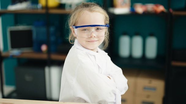 Suloinen blondi tyttö opiskelija hymyilee luottavainen seisoo kädet ristissä ele laboratoriossa luokkahuoneessa - Valokuva, kuva