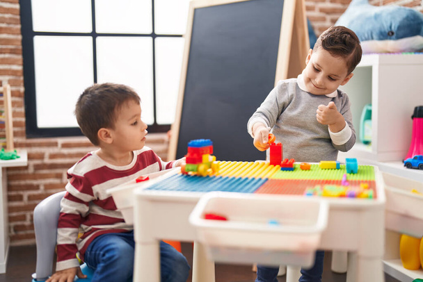Двоє дітей, які грають з будівельними блоками, сидять на столі в дитячому саду
 - Фото, зображення
