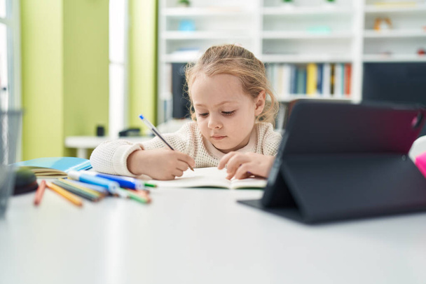 Schattige blonde meisje student met behulp van touchpad schrijven op notebook in de klas - Foto, afbeelding